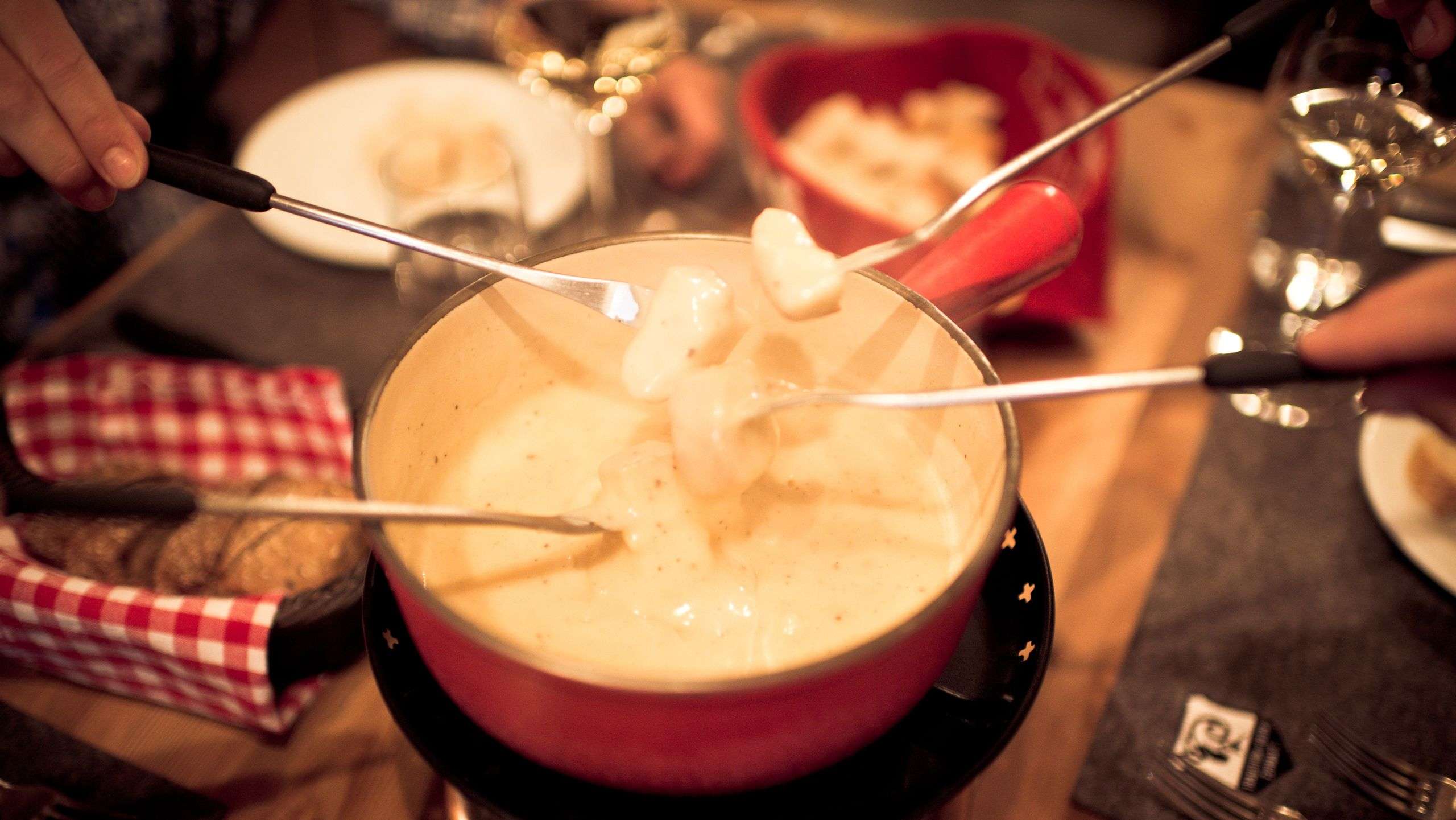 Plusieurs fourchettes plongent des morceaux de pain dans un caquelon à fondue rempli de fromage fondu.