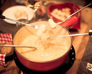 Mehrere Gabeln heben Brotstücke aus einem Fondue-Topf mit geschmolzenem Käse.