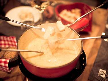 Plusieurs fourchettes soulèvent des morceaux de pain d’une marmite de fondue au fromage.