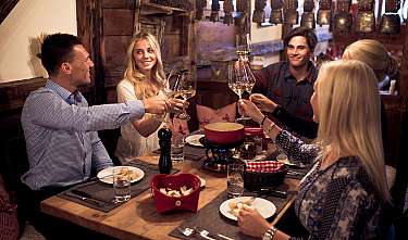 Sechs Freunde stoßen mit Weingläsern an einem gedeckten Tisch mit Fondue im Restaurant an.