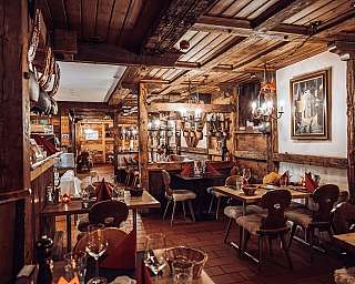 Gemütliches, rustikales Restaurant mit Holzbalken, gedeckten Tischen und warmer Beleuchtung.