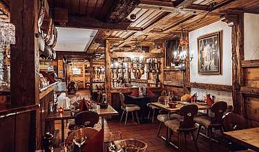 Gemütliches Restaurant mit Holzbalken, gedeckten Tischen und warmen Wandlampen.