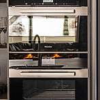 Stapel aus modernen Miele-Backöfen und Geräten in einer Küche.