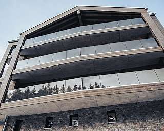 Bâtiment à plusieurs étages avec bardage en bois, balcons en verre et soubassement en pierre