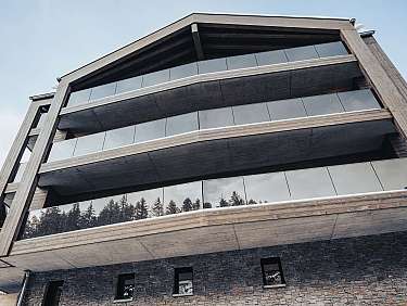 Façade moderne de bâtiment à plusieurs étages avec bois, balcons en verre et socle en pierre.