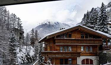 Holzchalet mit Schnee vor bergiger Winterlandschaft und Tannen