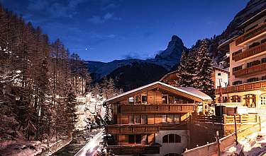 Chalets illuminés dans un village de montagne enneigé la nuit.