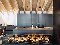 Cuisine moderne avec des armoires grises, un plafond en bois et une cheminée allumée au premier plan.