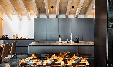 Moderne Küche mit Holzdecke, grauen Schränken und offenem Kamin im Vordergrund.