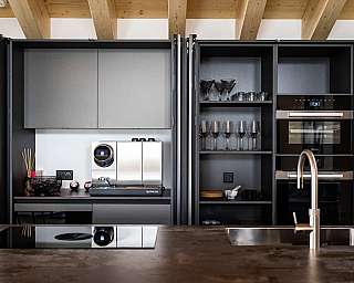 Cuisine moderne avec des armoires sombres, des verres, une machine à café et un four encastré.