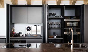 Moderne Küche mit dunklen Schränken, Espressomaschine, Weingläsern und Einbauöfen.