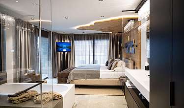 Chambre à coucher moderne avec lit double, télévision, grands rideaux et espace salle de bain luxueux.