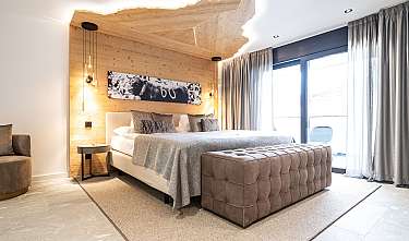 Modernes Schlafzimmer mit Doppelbett, Holzakzentwand, großen Fenstern und gepolsterter Bank am Bettende.