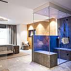 Helles Hotelzimmer mit Glasdusche, Bett und Fensterfront