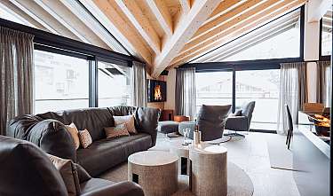 Modernes Wohnzimmer mit dunklen Sofas, großen Fenstern, Holzdecke und Kamin
