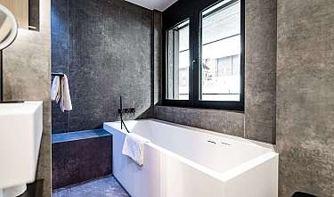 Modernes Bad mit weißer Badewanne, dunklen Wänden und großem Fenster