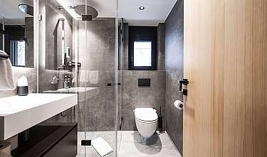 Modernes Badezimmer mit Glasdusche, wandhängendem WC und weißem Waschtisch in grauen Tönen, teilweiser Holztür