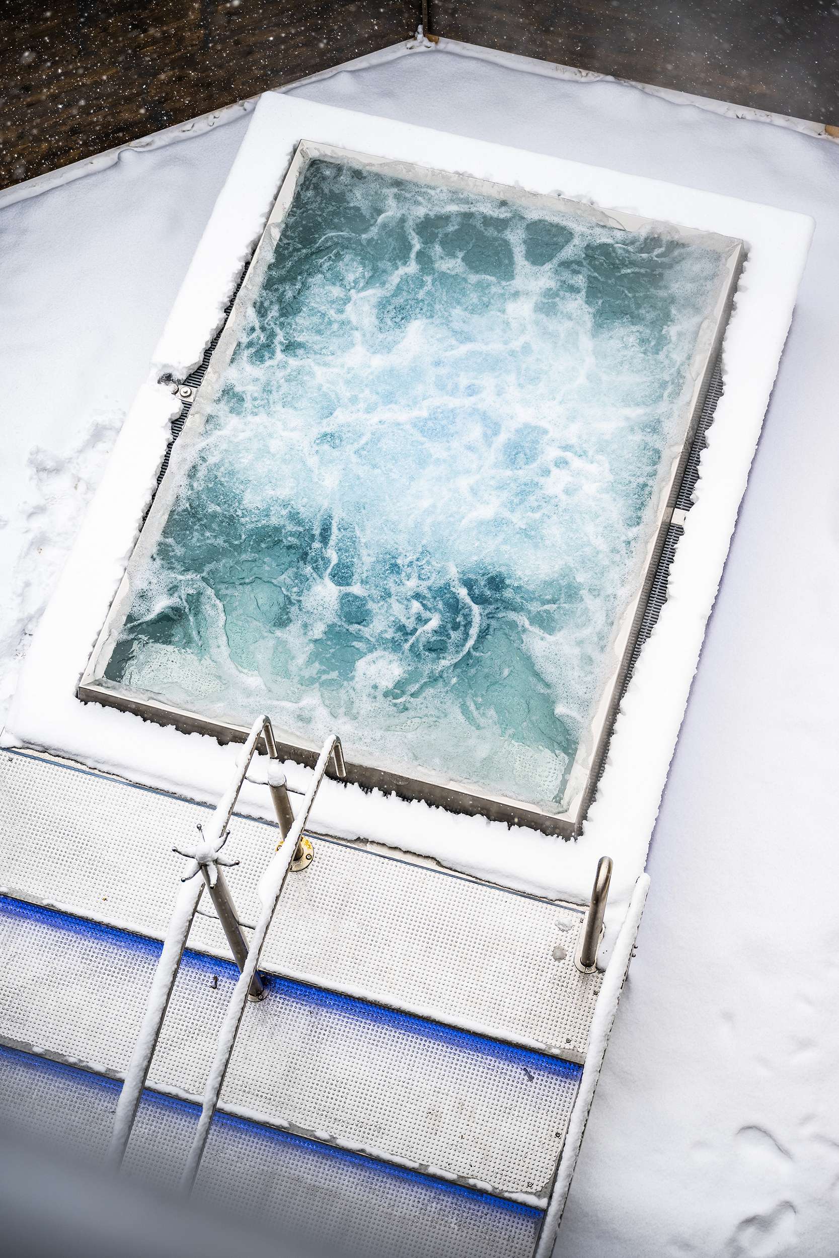 Terrasse recouverte de neige avec un jacuzzi rectangulaire et de l'eau chaude