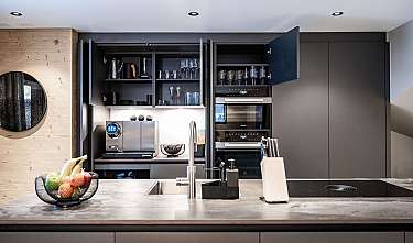 Moderne Küche mit offener Insel, Obstschale, Kaffeemaschine und eingebauten Schränken mit Gläsern und Geräten.,
