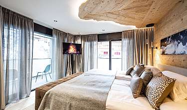 Chambre lumineuse avec grand lit, plafond en bois, rideaux et télévision avec image de cheminée.