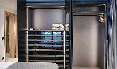 Modernes Schlafzimmer mit offenem Einbauschrank, Bett und gefalteten Handtüchern im Fach oben rechts