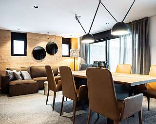 Modernes Esszimmer mit großem Holztisch, braunen Stühlen, Sofa und schwarzen Pendelleuchten.