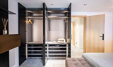 Moderne Ankleide mit offenem Kleiderschrank, Holztür und gepolsterter Sitzbank im Schlafzimmerbereich