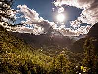 Vallée de montagne baignée de soleil avec un sommet enneigé, des nuages et une forêt
