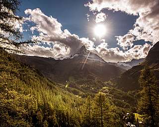 Paysage de montagne ensoleillé avec sommet, nuages et vallée boisée