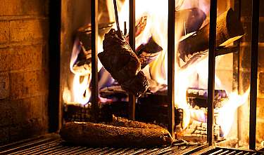 Fleischstücke grillen über offenen Flammen in einem Feuerraum.
