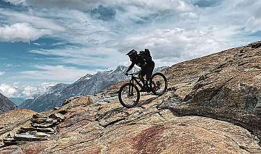 Mountainbiker fährt auf felsigem Berggrat unter dramatischem Himmel.