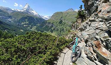 Mountainbike an schmalem Felsenweg mit Blick auf alpine Berge und Tal