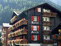 Traditionelles Berghotel mit roten Fensterläden und blumengeschmückten Balkonen vor bewaldeten Bergen.