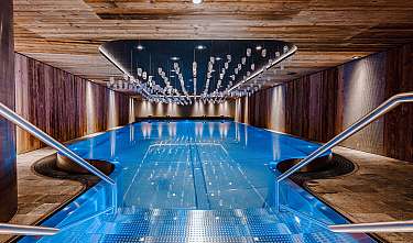 Moderner Innenpool mit blauer Wasserfläche, Holzverkleidung und Glasdeko an der Decke.