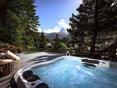 Jacuzzi sur terrasse en bois avec serviettes, entouré d'arbres et d'un panorama de montagne.