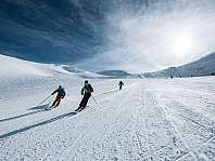 Trois skieurs descendent une large piste enneigée sous un ciel bleu.
