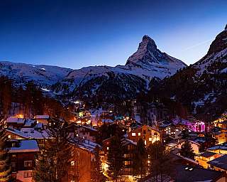 Zermatt enneigé la nuit avec des maisons illuminées et le Cervin en arrière-plan