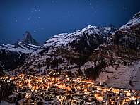 Village de montagne illuminé entre des sommets enneigés sous une nuit étoilée.