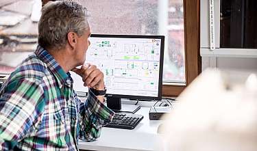 Ein Mann sitzt am Schreibtisch vor einem Monitor mit einem technischen Diagramm.