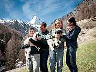 Quatre personnes tiennent deux moutons devant un paysage de montagne enneigé.