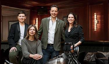 Four people pose in an elegant room next to a motorcycle.
