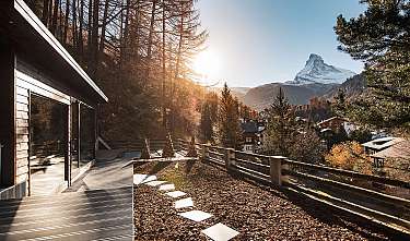 Holzterrasse mit Blick auf ein Bergdorf und einen schneebedeckten Gipfel.