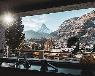 Blick auf ein Bergdorf mit markantem Gipfel und Sonne im Fensterrahmen.
