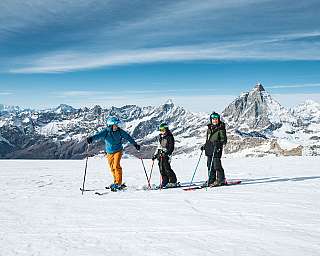 Trois skieurs se tiennent sur un sommet enneigé devant des montagnes alpines.