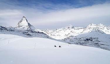 Schneebedeckte Berge unter blauem Himmel mit weitem weißen Hang und zwei kleinen Personen.