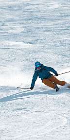 Ein Skifahrer fährt eine steile, verschneite Abfahrt mit Schwung und Schneeaufwirbelung.