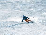 Un skieur descend une piste raide et enneigée avec élan et projection de neige.
