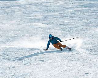 Un skieur descend une pente raide enneigée en soulevant un nuage de neige.