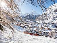 Village enneigé dans la vallée devant un sommet montagneux emblématique.