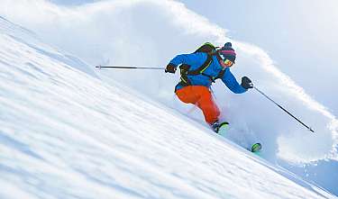 Un skieur en veste bleue et pantalon orange descend dans la poudreuse fraîche.